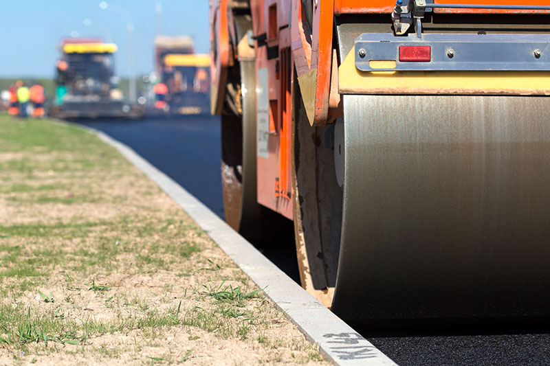 Road roller compacting asphalt near curb stone